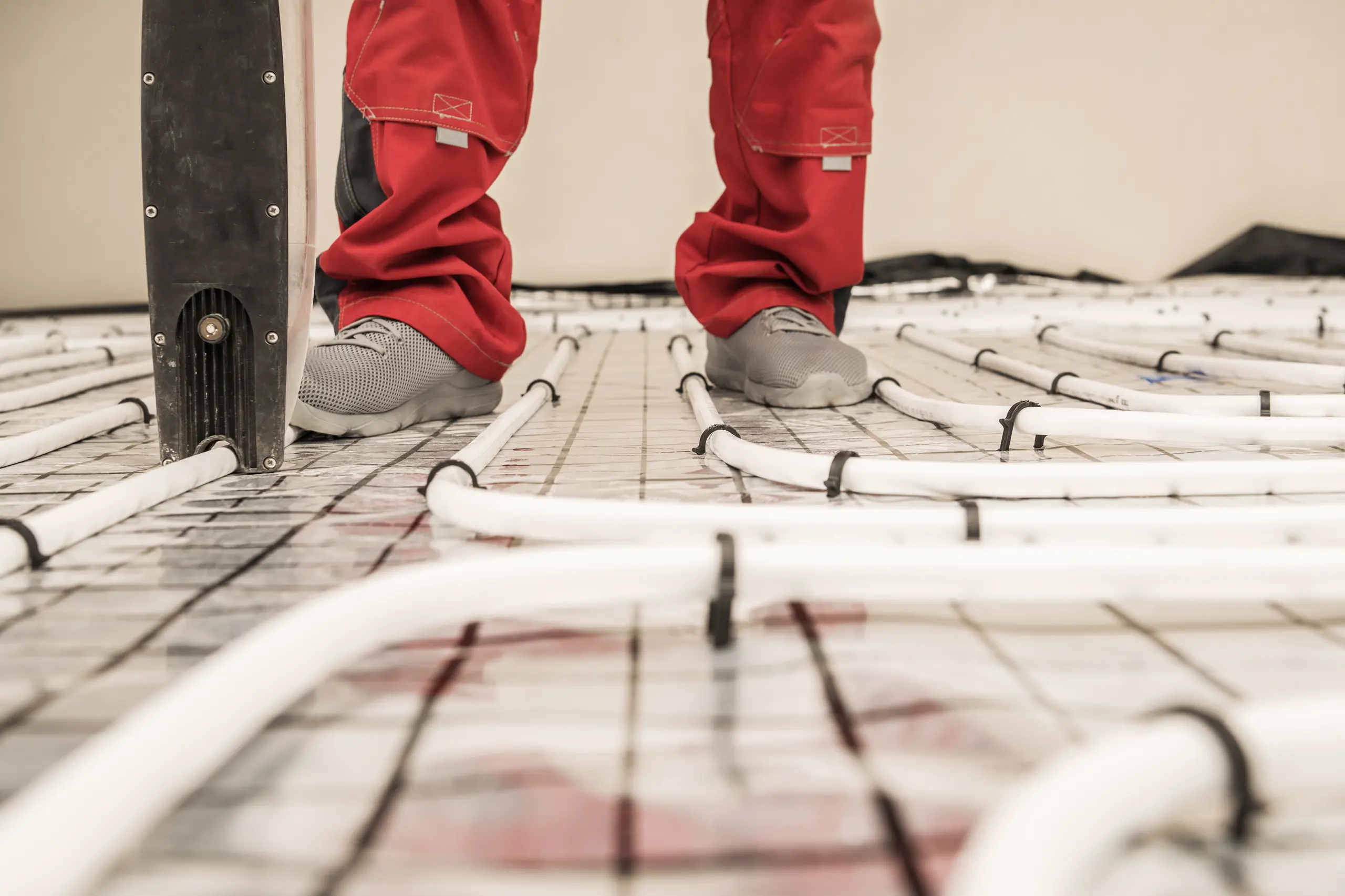 Instalacja ogrzewania podłogowego, osoba w czerwonych spodniach stająca na rurach