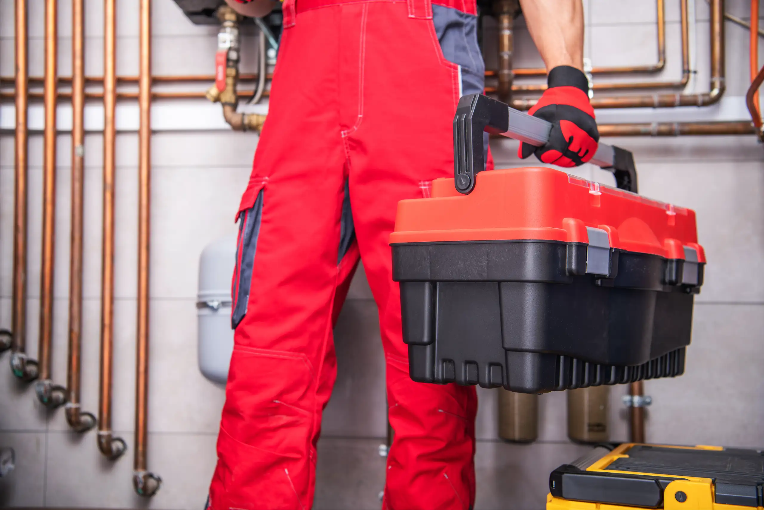 Hydraulik w czerwonych ubraniach trzyma skrzynkę narzędziową w pobliżu instalacji wodno-kanalizacyjnej